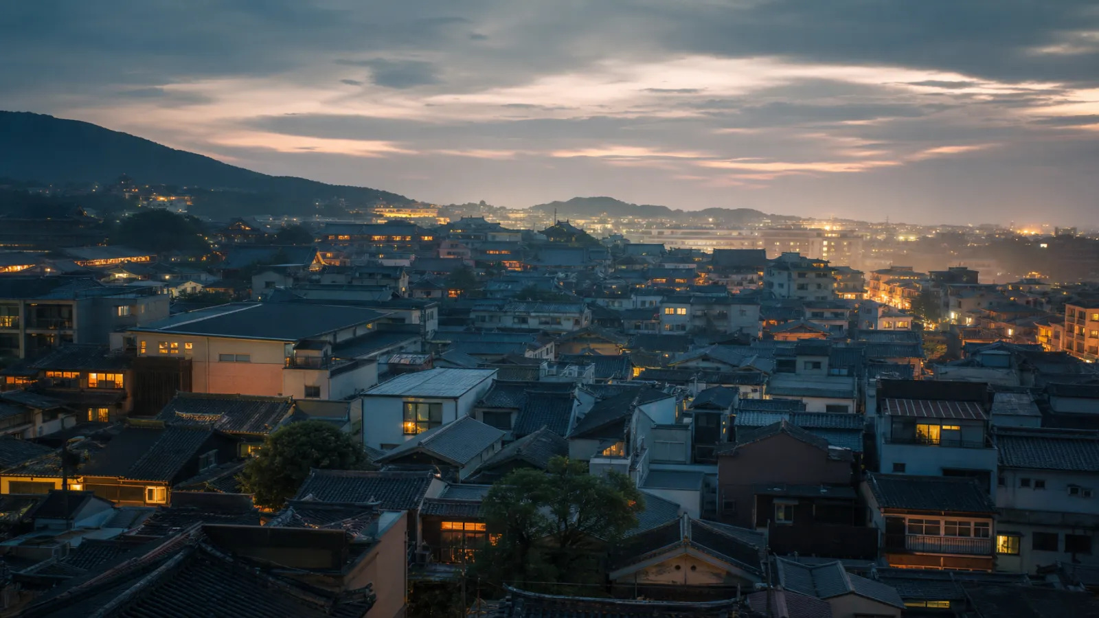 Soft twilight sky over layered Asian city rooftops with warm window lights and calm blue-grey atmosphere