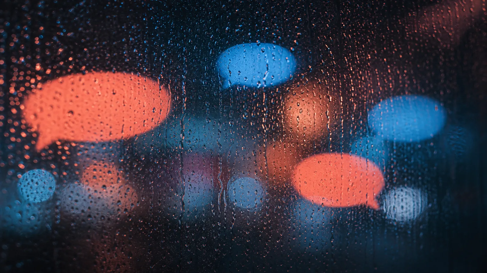 Rain-streaked night window with soft coral and blue city light reflections
